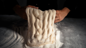 Човек приготвя тесто за пинса и я разтегля на ръце